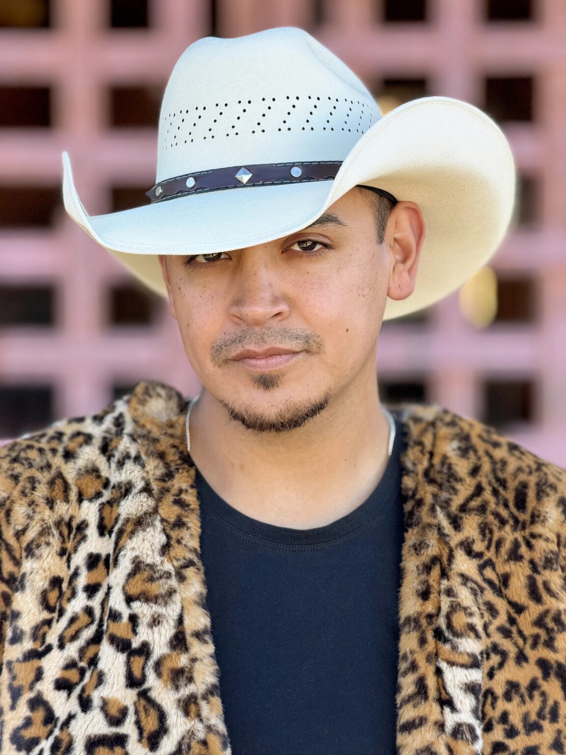 Close-up portrait of a man in a white cowboy hat and leopard-print coat.