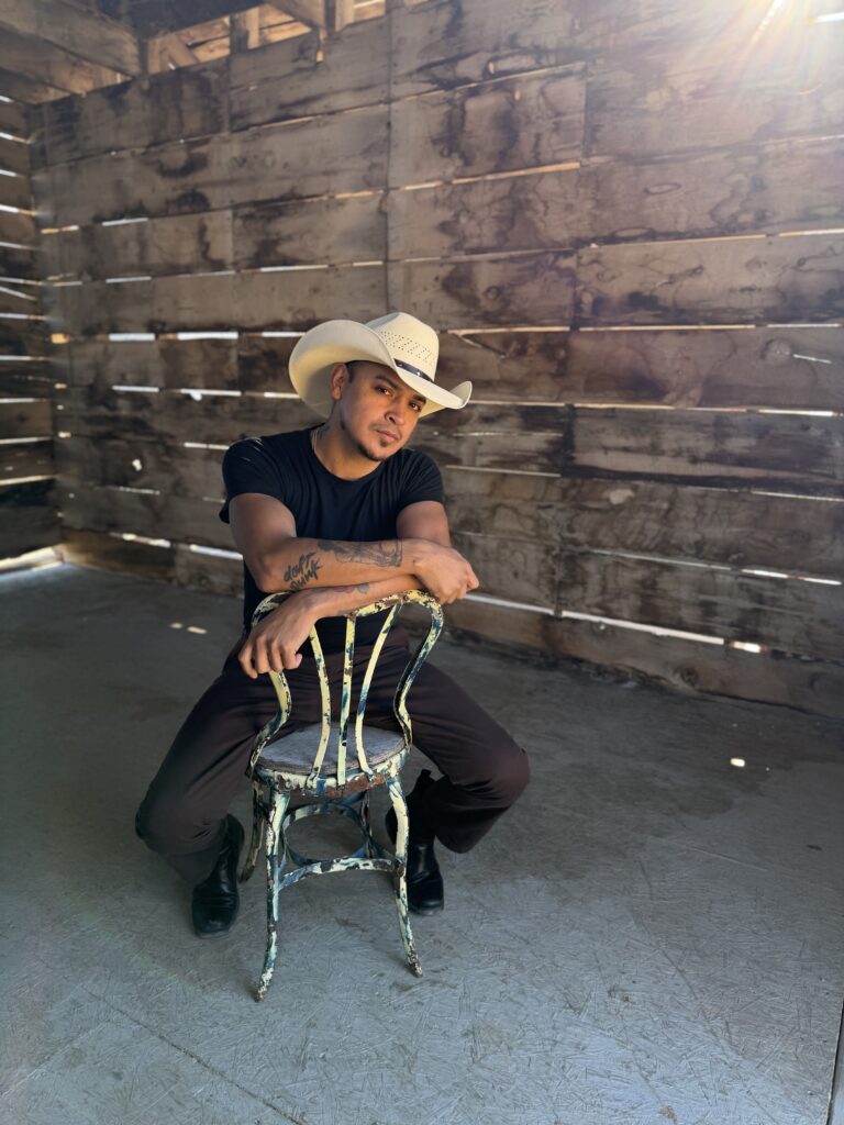 Personal brand portrait of a man in a white cowboy hat seated backward on a vintage chair in a rustic setting.